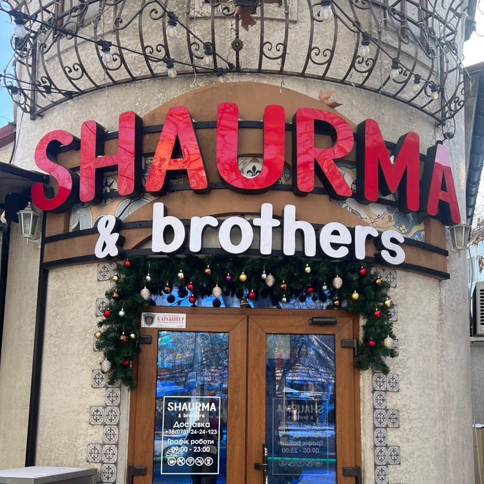 Вивіска «SHAURMA & brothers» над входом до закладу, під нею новорічна гірлянда з кульками та хвоєю, скляні двері